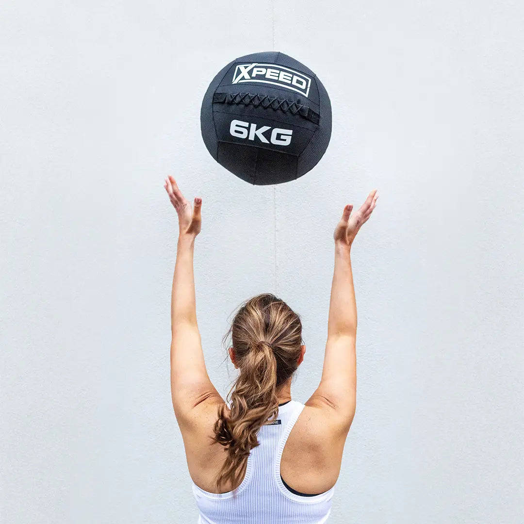 Woman in active wear throwing a wall ball against white wall.