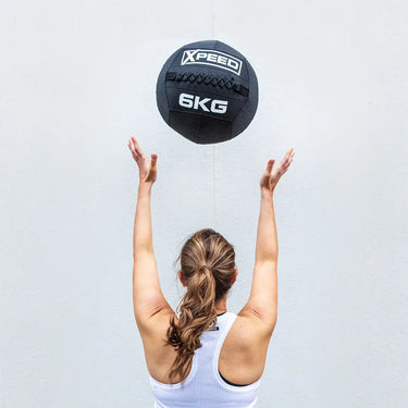 Woman in active wear throwing a wall ball against white wall.