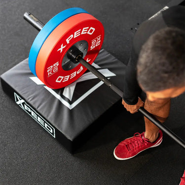 Man training with barbell and bumper plates on drop pads in home gym.